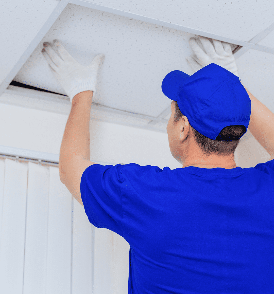 Worker adjusting ceiling tiles with gloves.